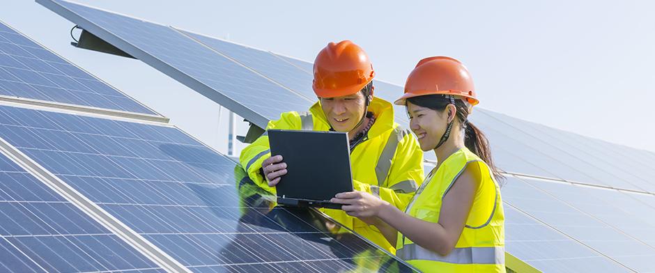 Man 和 woman reviewing a laptop screen next to a set of industrial-scale solar panels.